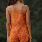 woman with brown hair wearing an orange overall style romper with rumi bandeau underneath with puakenikeni print