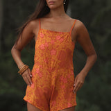 woman with brown hair wearing an orange overall style romper with rumi bandeau underneath with puakenikeni print