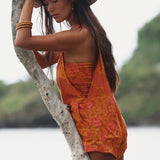 woman with brown hair wearing an orange overall style romper with rumi bandeau underneath with puakenikeni print