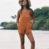 woman with brown hair wearing an orange overall style romper with rumi bandeau underneath with puakenikeni print