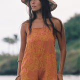woman with brown hair wearing an orange overall style romper with rumi bandeau underneath with puakenikeni print