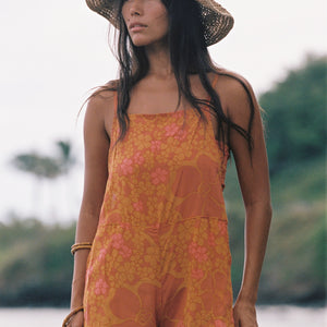 woman with brown hair wearing an orange overall style romper with rumi bandeau underneath with puakenikeni print