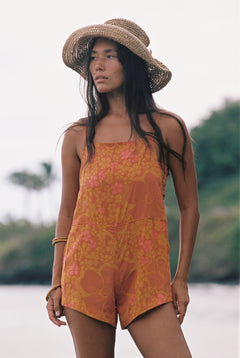 woman with brown hair wearing an orange overall style romper with rumi bandeau underneath with puakenikeni print