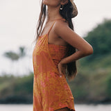 woman with brown hair wearing an orange overall style romper with rumi bandeau underneath with puakenikeni print