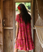 A woman with dark hair wears a YIREH tiered flowy dress. It is the Florentine Dress in the Garden 'Awapuhi print. 