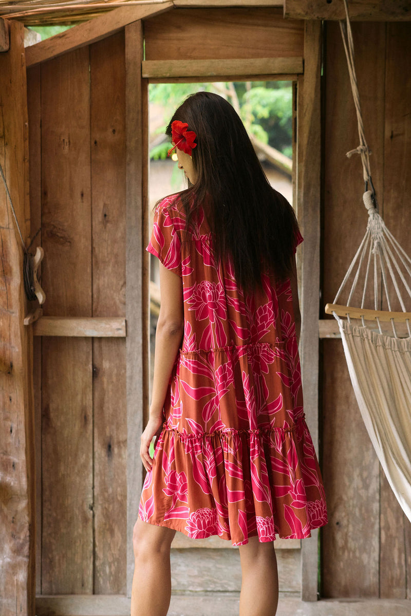 A woman with dark hair wears a YIREH tiered flowy dress. It is the Florentine Dress in the Garden 'Awapuhi print. 