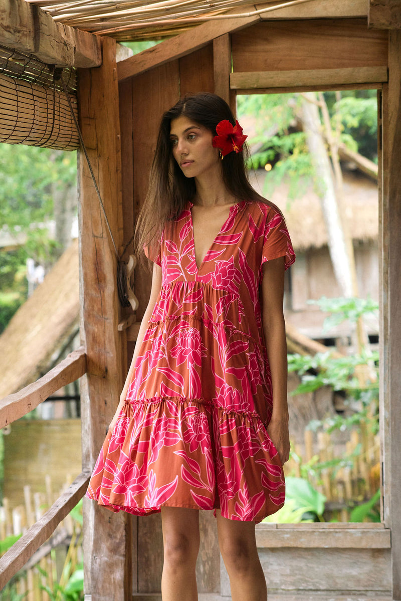 A woman with dark hair wears a YIREH tiered flowy dress. It is the Florentine Dress in the Garden 'Awapuhi print. 