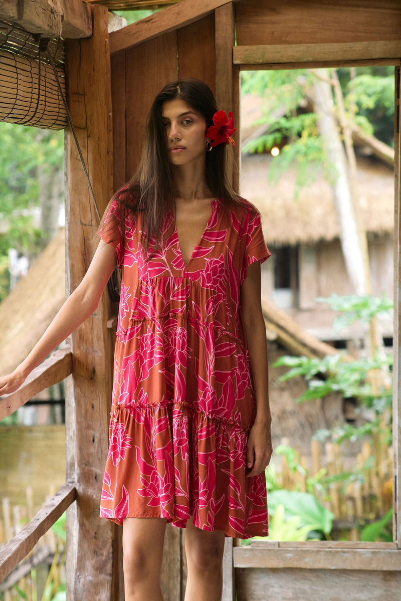 A woman with dark hair wears a YIREH tiered flowy dress. It is the Florentine Dress in the Garden 'Awapuhi print. 