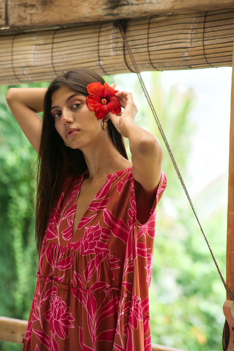 A woman with dark hair wears a YIREH tiered flowy dress. It is the Florentine Dress in the Garden 'Awapuhi print. 