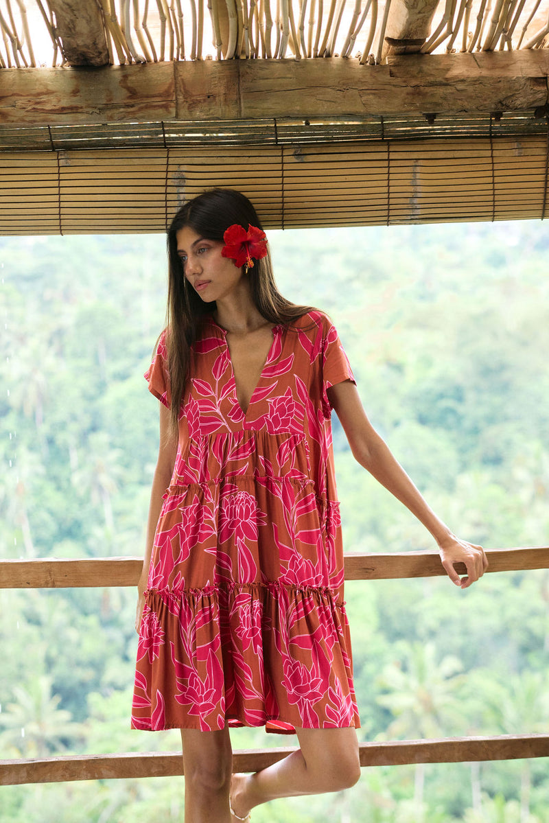 A woman with dark hair wears a YIREH tiered flowy dress. It is the Florentine Dress in the Garden 'Awapuhi print. 