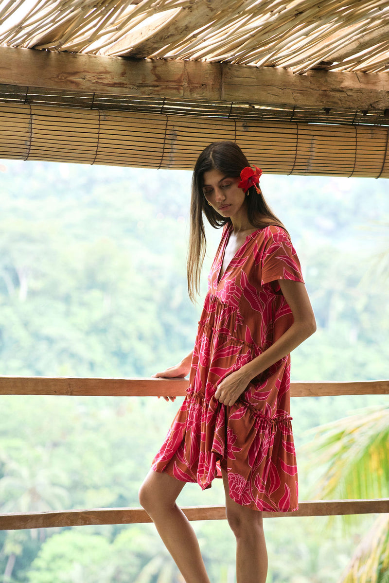 A woman with dark hair wears a YIREH tiered flowy dress. It is the Florentine Dress in the Garden 'Awapuhi print. 