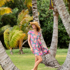 woman with brown hair wearing a teal v neck flowy dress with orange and pink floral print