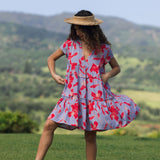 woman with brown hair wearing a flowy dress with periwinkle background and bright red hibiscus print.