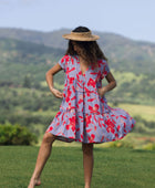 woman with brown hair wearing a flowy dress with periwinkle background and bright red hibiscus print.