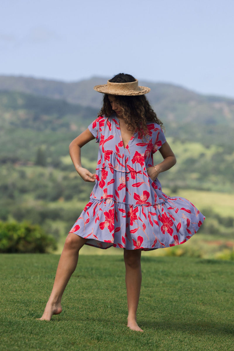 woman with brown hair wearing a flowy dress with periwinkle background and bright red hibiscus print.
