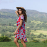 woman with brown hair wearing a flowy dress with periwinkle background and bright red hibiscus print.
