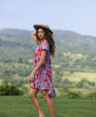 woman with brown hair wearing a flowy dress with periwinkle background and bright red hibiscus print.