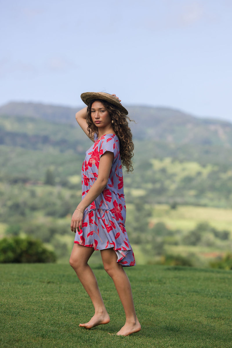 woman with brown hair wearing a flowy dress with periwinkle background and bright red hibiscus print.