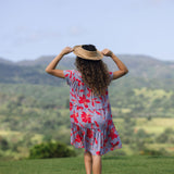 woman with brown hair wearing a flowy dress with periwinkle background and bright red hibiscus print.