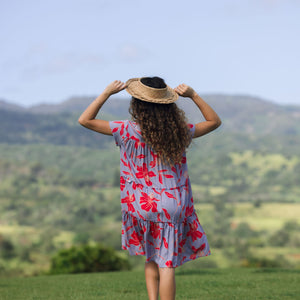 woman with brown hair wearing a flowy dress with periwinkle background and bright red hibiscus print.