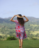 woman with brown hair wearing a flowy dress with periwinkle background and bright red hibiscus print.