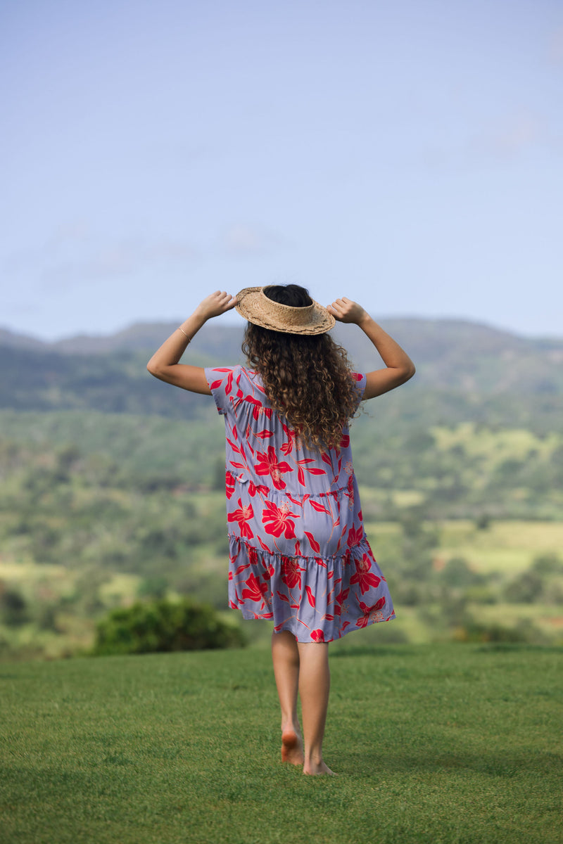 woman with brown hair wearing a flowy dress with periwinkle background and bright red hibiscus print.