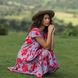 woman with brown hair wearing a flowy dress with periwinkle background and bright red hibiscus print.