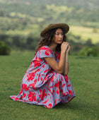 woman with brown hair wearing a flowy dress with periwinkle background and bright red hibiscus print.