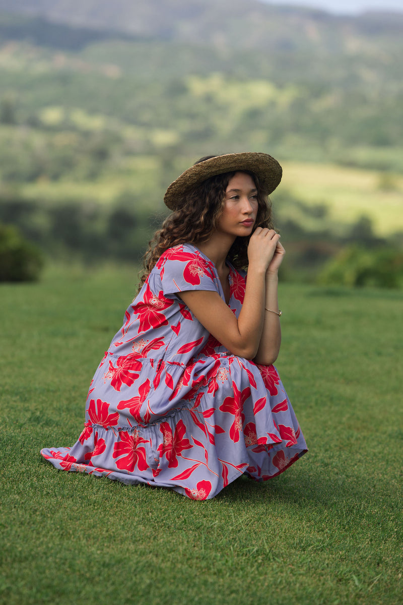 woman with brown hair wearing a flowy dress with periwinkle background and bright red hibiscus print.