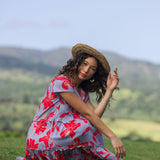 woman with brown hair wearing a flowy dress with periwinkle background and bright red hibiscus print.