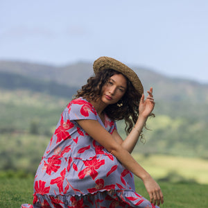 woman with brown hair wearing a flowy dress with periwinkle background and bright red hibiscus print.