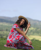 woman with brown hair wearing a flowy dress with periwinkle background and bright red hibiscus print.