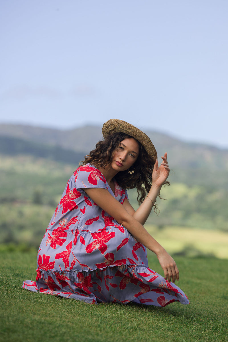 woman with brown hair wearing a flowy dress with periwinkle background and bright red hibiscus print.