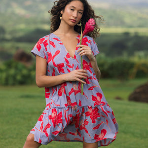 woman with brown hair wearing a flowy dress with periwinkle background and bright red hibiscus print.