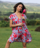 woman with brown hair wearing a flowy dress with periwinkle background and bright red hibiscus print.