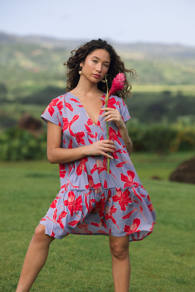 woman with brown hair wearing a flowy dress with periwinkle background and bright red hibiscus print.