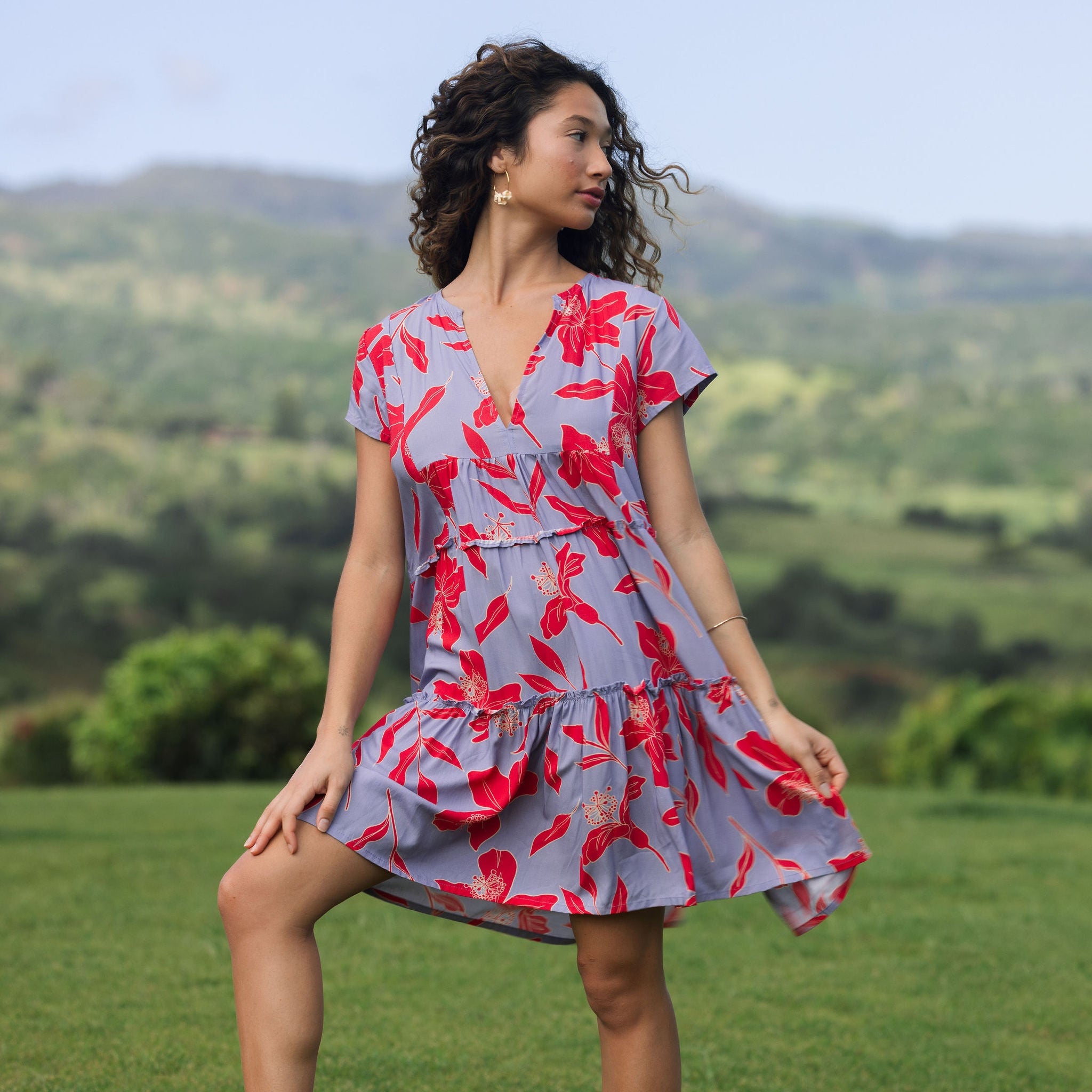 woman with brown hair wearing a flowy dress with periwinkle background and bright red hibiscus print.