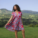 woman with brown hair wearing a flowy dress with periwinkle background and bright red hibiscus print.