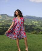 woman with brown hair wearing a flowy dress with periwinkle background and bright red hibiscus print.