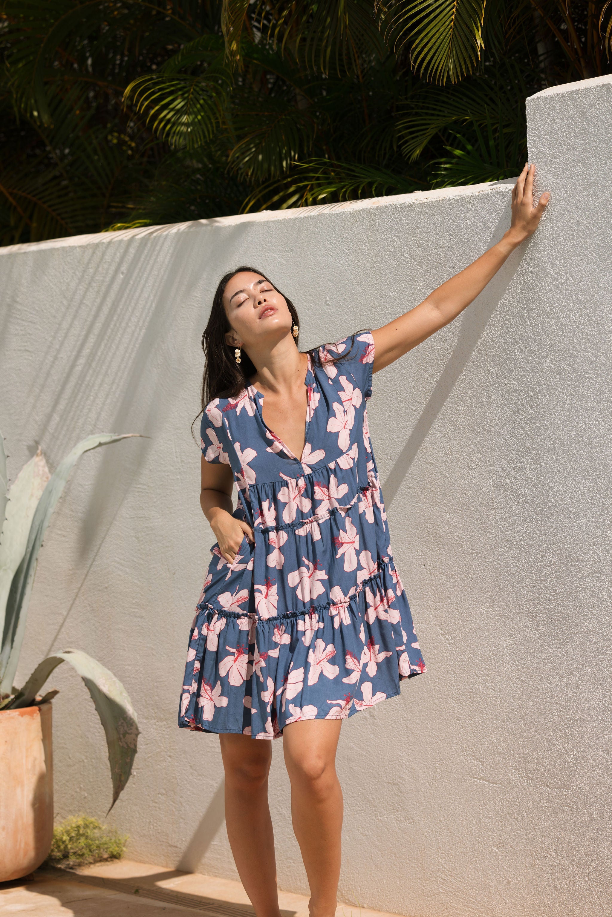 woman with black hair wearing a mini tiered dress in a navy color with pink hibiscus blossoms 