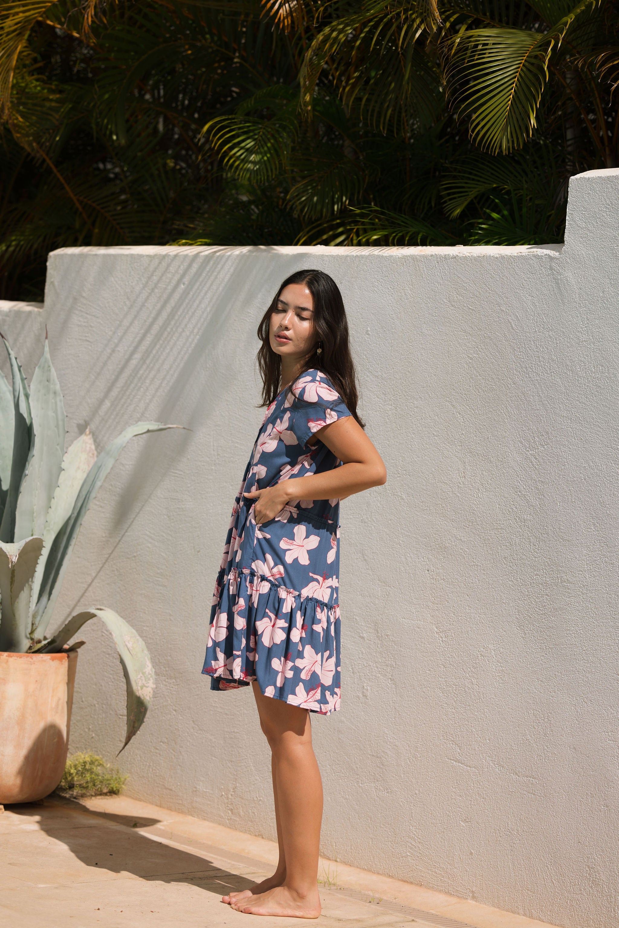 woman with black hair wearing a mini tiered dress in a navy color with pink hibiscus blossoms 
