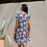 woman with black hair wearing a mini tiered dress in a navy color with pink hibiscus blossoms 