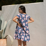 woman with black hair wearing a mini tiered dress in a navy color with pink hibiscus blossoms 