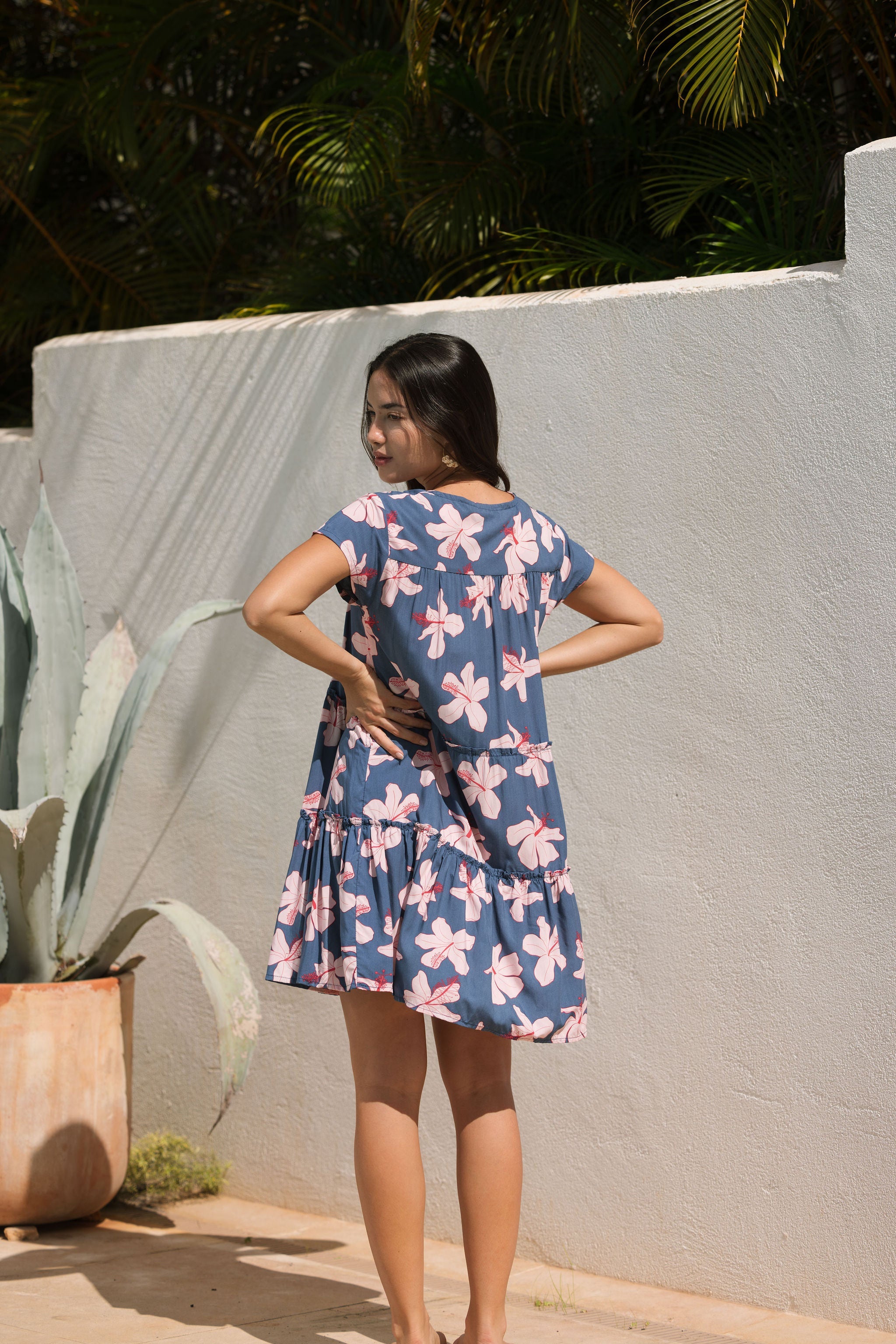 woman with black hair wearing a mini tiered dress in a navy color with pink hibiscus blossoms 