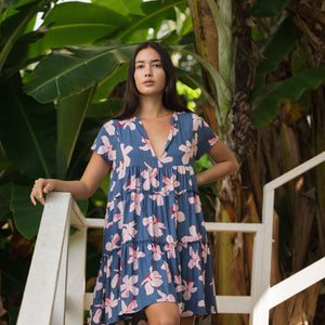 woman with black hair wearing a mini tiered dress in a navy color with pink hibiscus blossoms 