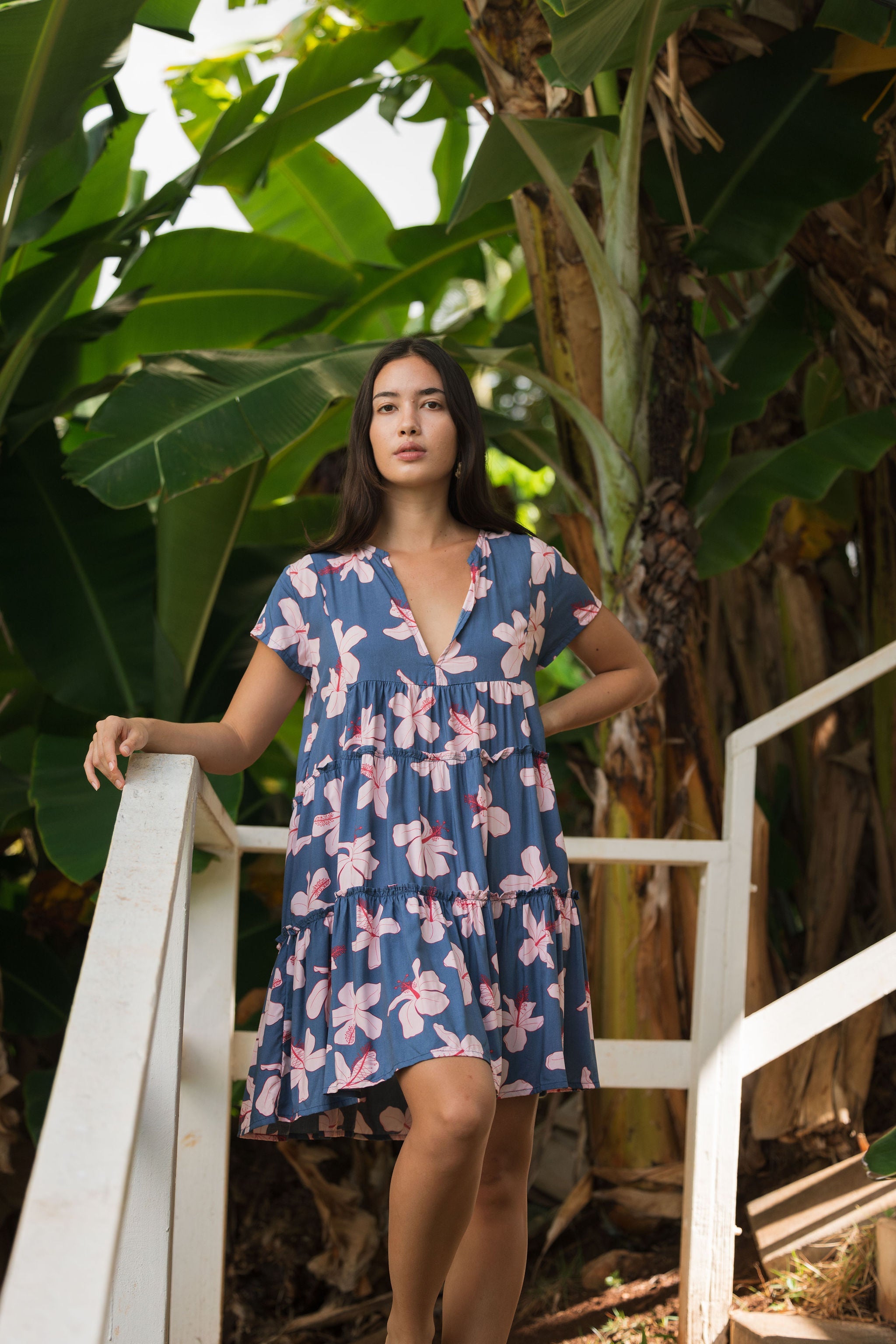 woman with black hair wearing a mini tiered dress in a navy color with pink hibiscus blossoms 