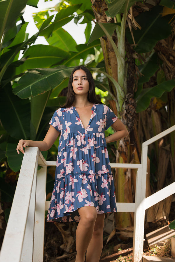 woman with black hair wearing a mini tiered dress in a navy color with pink hibiscus blossoms 