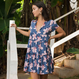 woman with black hair wearing a mini tiered dress in a navy color with pink hibiscus blossoms 