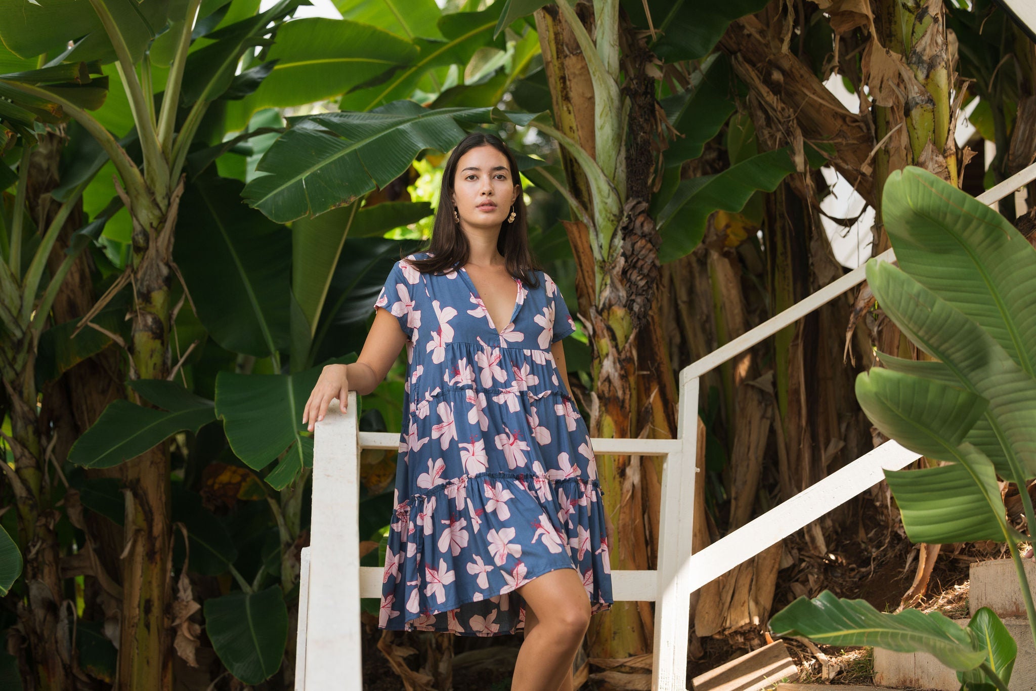 woman with black hair wearing a mini tiered dress in a navy color with pink hibiscus blossoms 