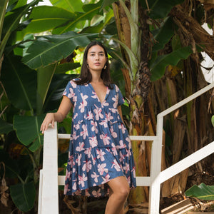 woman with black hair wearing a mini tiered dress in a navy color with pink hibiscus blossoms 